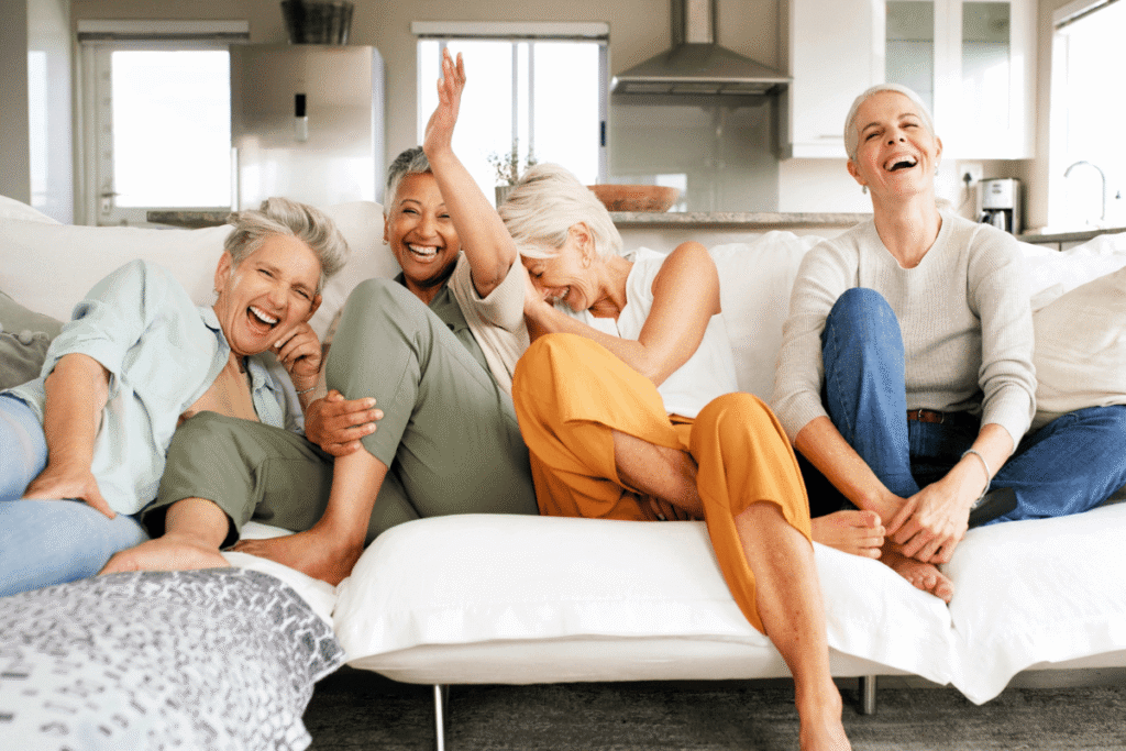 Mature, happy women watching TV on the sofa, laughing at a funny joke, a comedy movie, or a show at home.